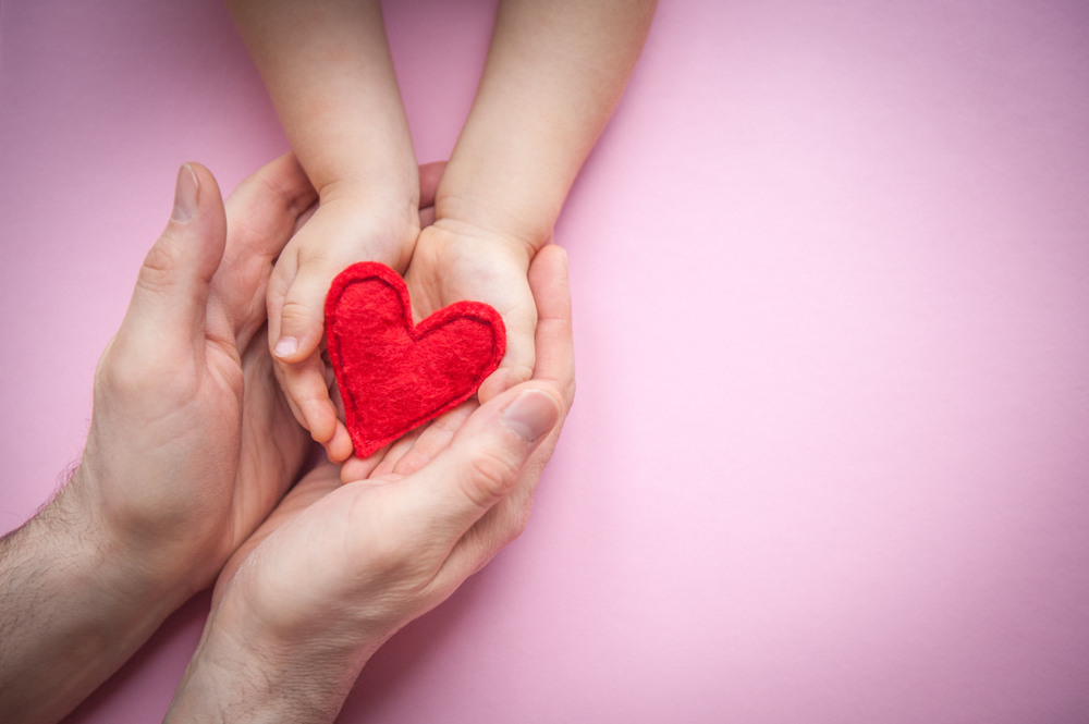 Father holding his childs hands with a plush heart in the middle